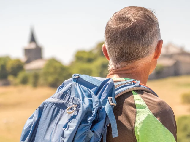 Hiker on the Chemin de St Regis with the church of Saint-Jeures in the distance